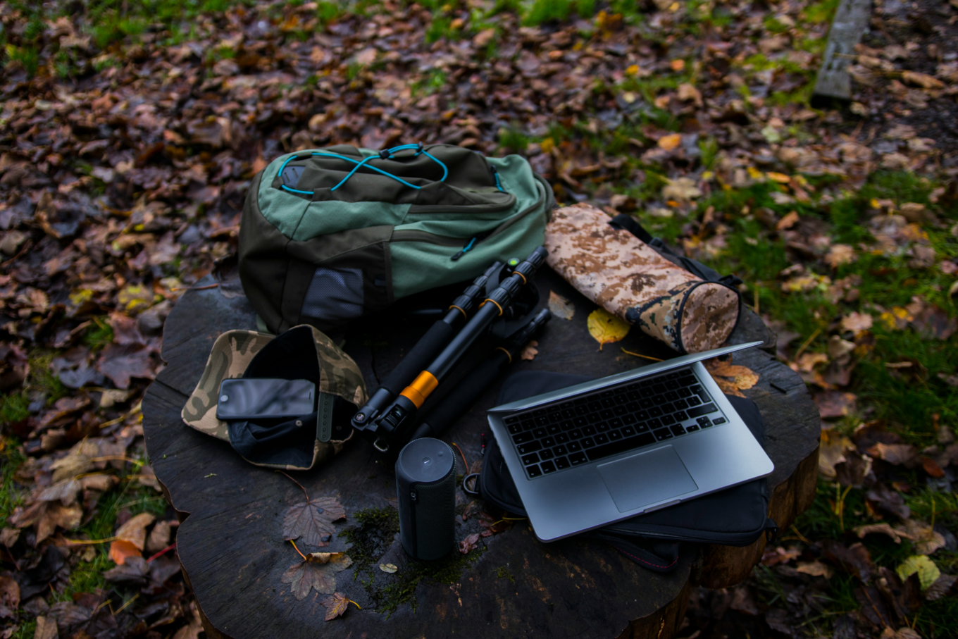 Outdoor gear and a laptop on a tree stump in an autumn forest